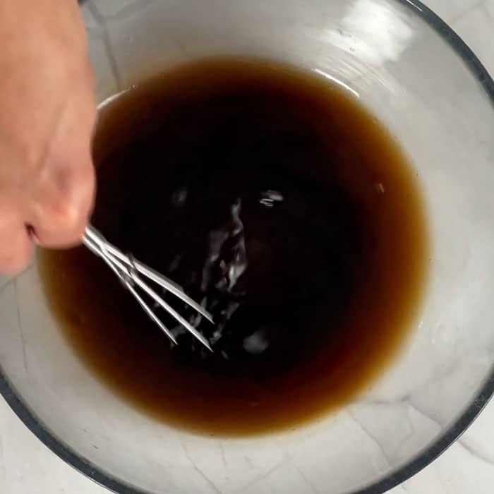 mixing marinade in a large glass bowl using a small whisk