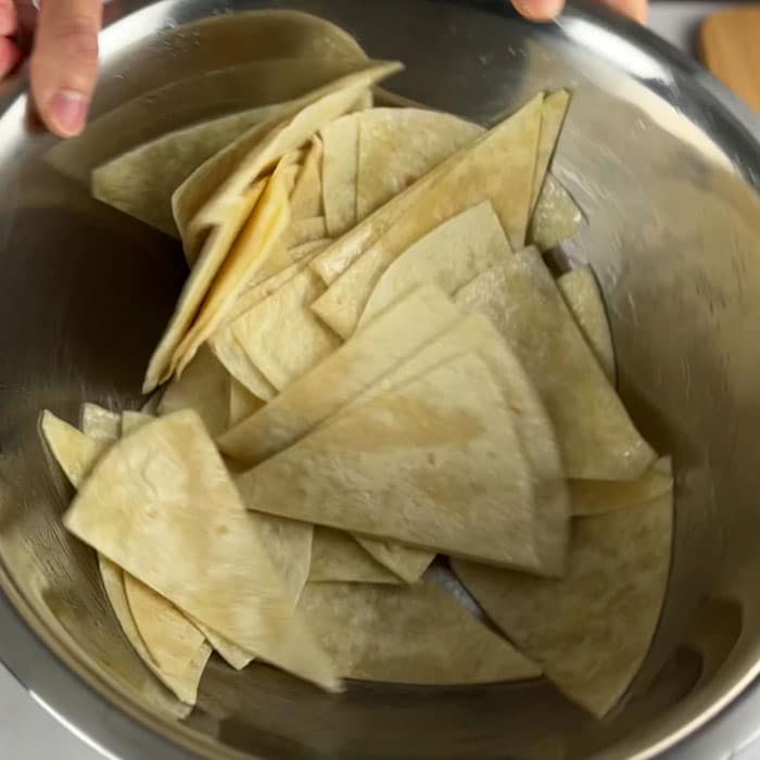 Coating sliced tortilla chips with oil.