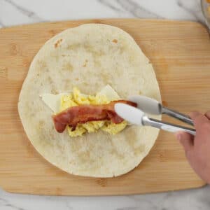 adding bacon on eggs with cheese on tortilla wrap