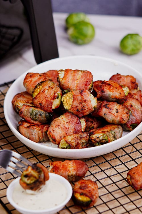 Bacon wrapped brussel sprouts air fryer recipe bite shot, served in a plate with ranch dipping sauce.