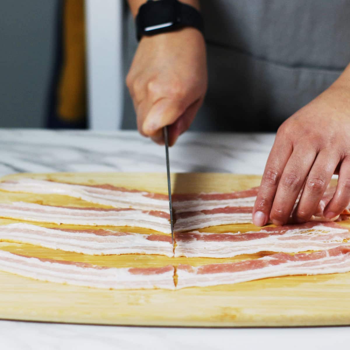 Slicing bacon in half on a bamboo chopping board