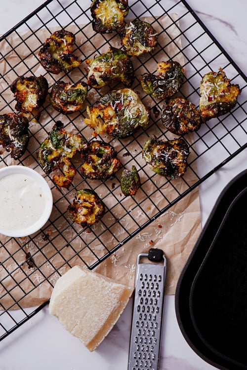 Smashed brussels sprouts air fryer recipe bite shot, served on a cooling rack with ranch dipping sauce.