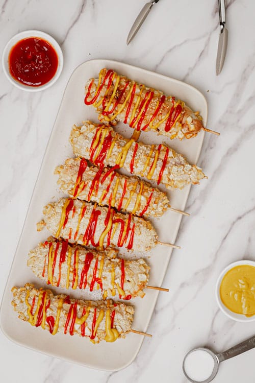 Air fryer Korean corn dog recipe bite shot, 6 korean cheese dogs on a serving plate with ketchup and mustard drizzle