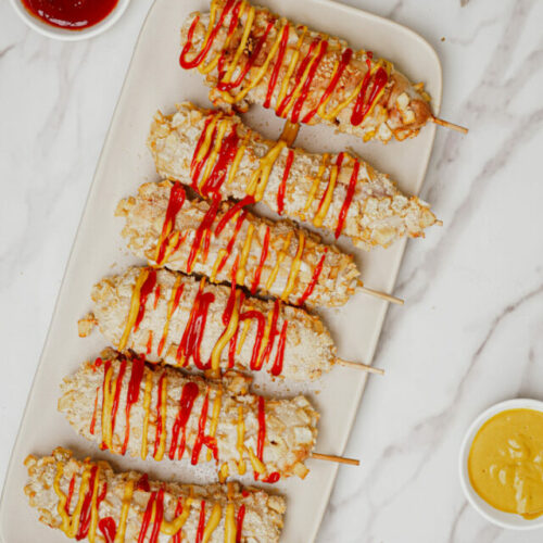 Air fryer Korean corn dog recipe bite shot, 6 korean cheese dogs on a serving plate with ketchup and mustard drizzle