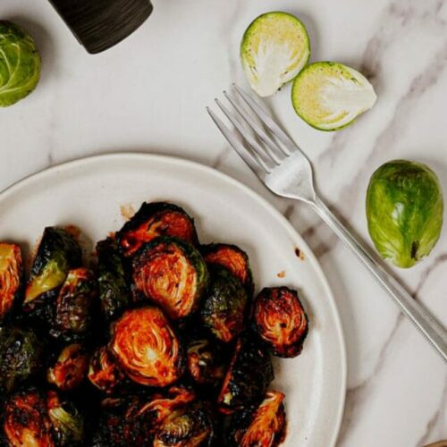 Honey sriracha Brussels sprouts air fryer recipe bite shot, served in a white plate with a fork on the side
