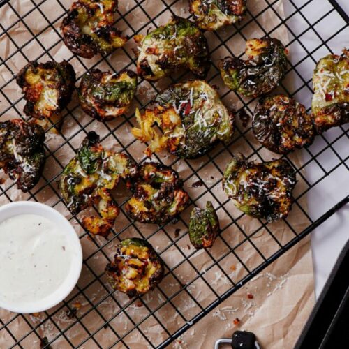 Smashed brussels sprouts air fryer recipe bite shot, served on a cooling rack with ranch dipping sauce.