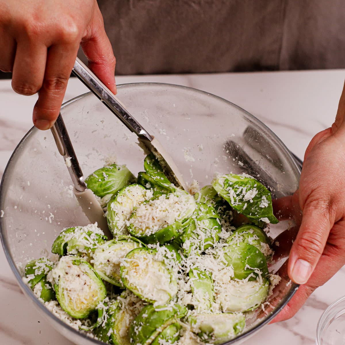 Seasoning Brussels sprouts with olive oil, salt, pepper, and lots of grated parmesan cheese.