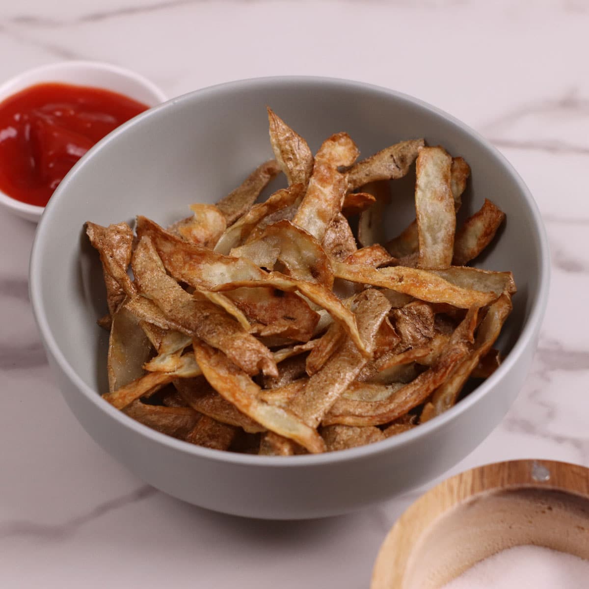 Air fried potato skin chips with ketchup on the side.