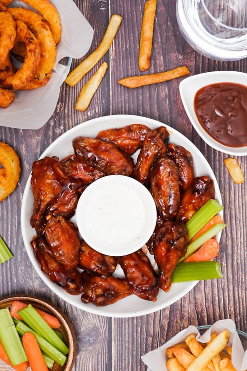 Air fryer BBQ chicken wings recipe bite shot, top view, served with sauce, celery, carrots, onion rings, soda and fries.
