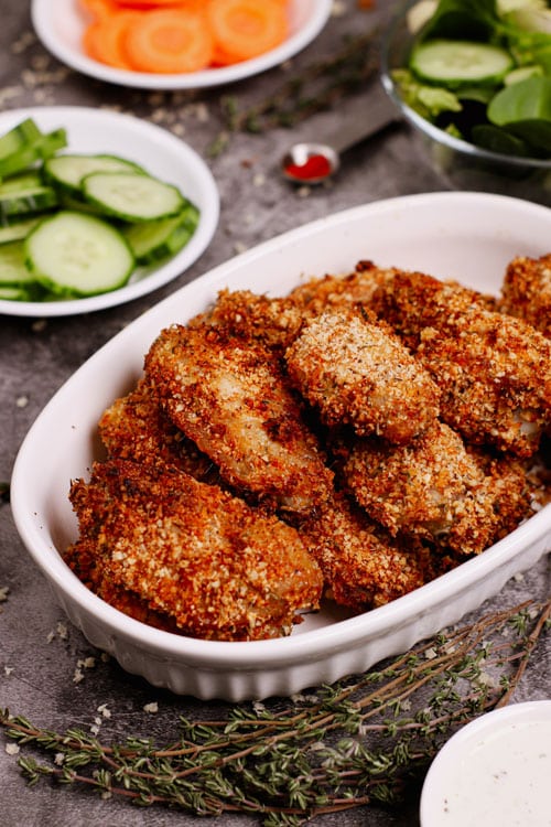 Air fryer breaded chicken wings recipe bite shot, with herbs and vegetables on the background.