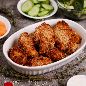 Air fryer breaded chicken wings recipe with herbs and vegetables on the background.