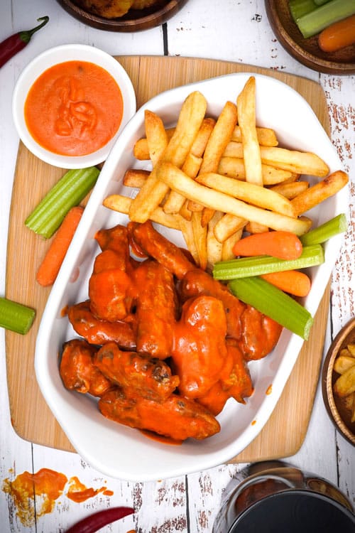 Air fryer Buffalo chicken wings recipe bite shot, served with fries, celery and carrots.