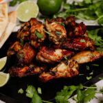 Air fryer cilantro lime chicken wings recipe bite shot, on a black serving board with limes and cilantro in the background.