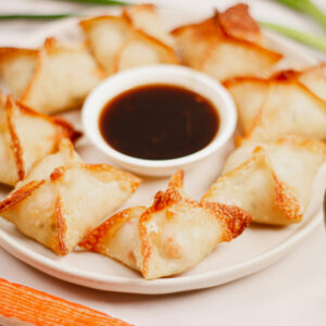 Air fryer crab rangoons served on a plate with a side of dipping sauce.