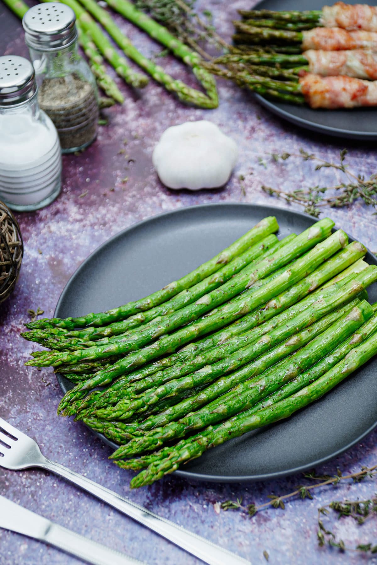 Air fryer garlic roasted asparagus recipe bite shot, served on a black plate with garlic on the background.