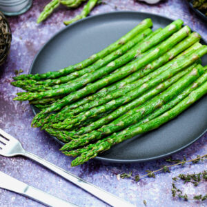 Air fryer garlic roasted asparagus served on a black plate with fork and knife.