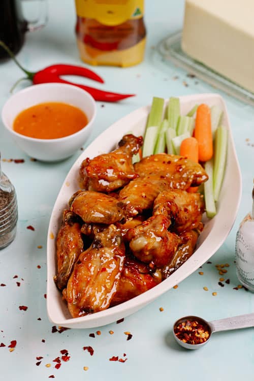 Air fryer honey hot wings recipe bite shot, served in a leaf-shaped serving dish with celery and carrot sticks on the side.