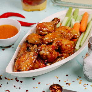 Air fryer honey hot wings, served in a leaf-shaped serving dish with celery and carrot sticks on the side.