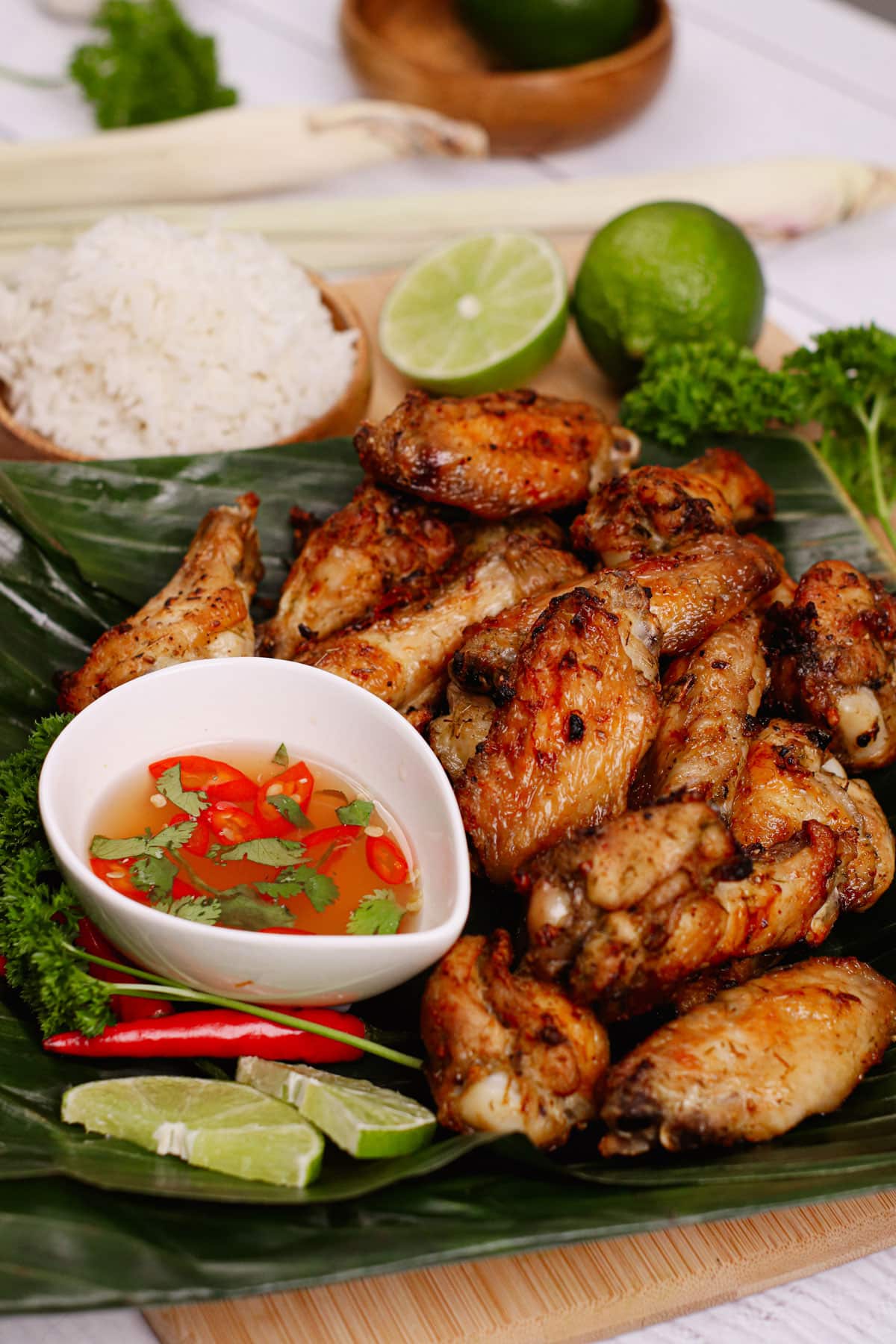 Air fryer lemongrass chicken wings recipe bite shot, served on a banana leaf with Thai savory and spicy dip and rice on the background.