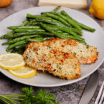 Air fryer parmesan crusted salmon with green beans and sliced lemons on the side.
