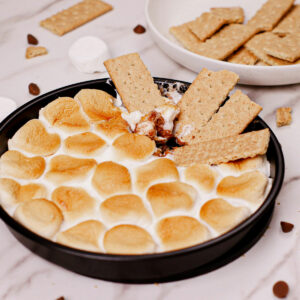Air fryer s'mores dip recipe served on a pizza pan, with graham crackers on the side.