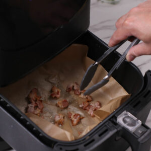 Step 4: Flipping bacon slices in air fryer with a pair of tongs.