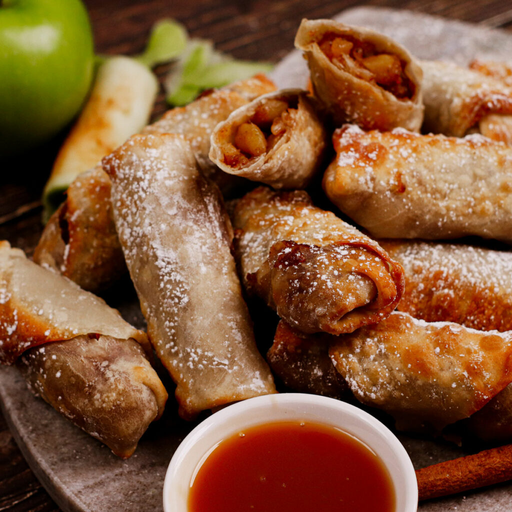 Air fryer apple pie egg rolls with powdered sugar on top and caramel dipping sauce.