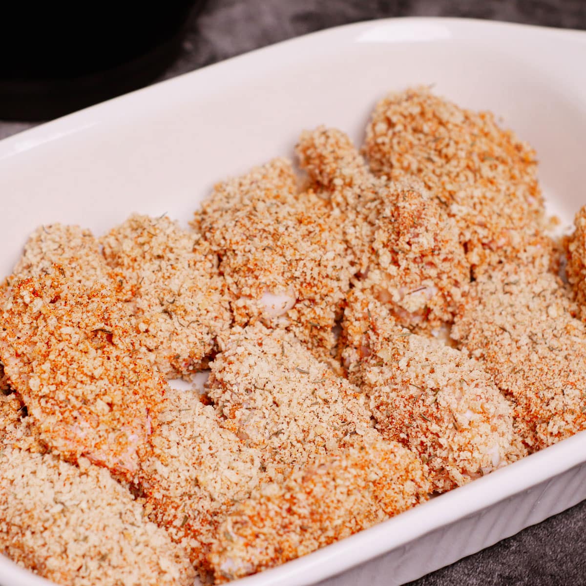Uncooked breaded chicken wings in a serving dish.