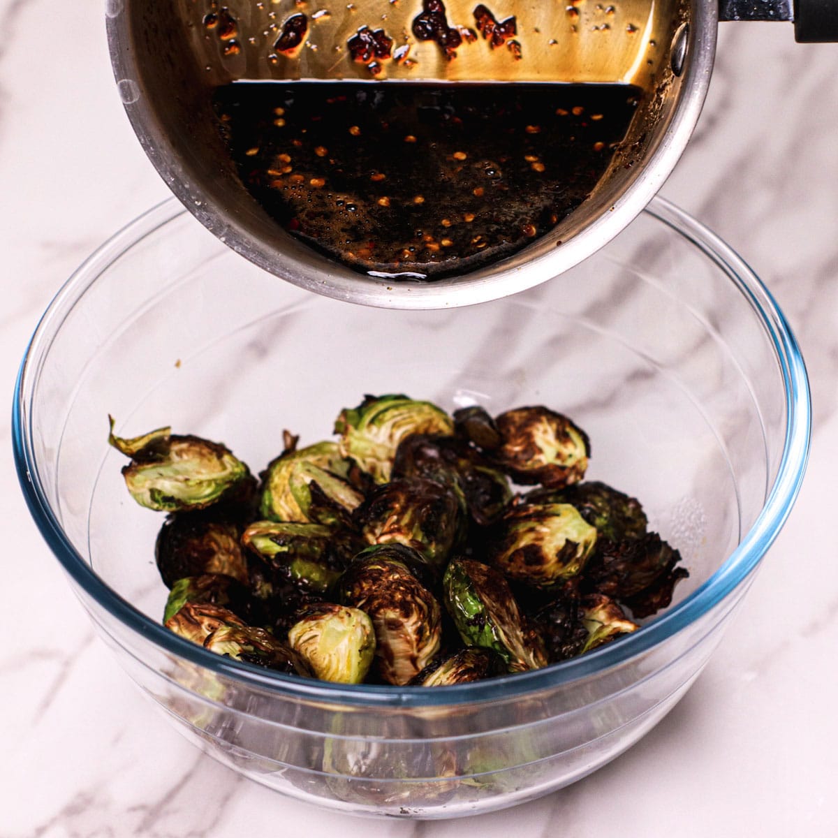 Adding honey garlic sauce to roasted Brussels sprouts.