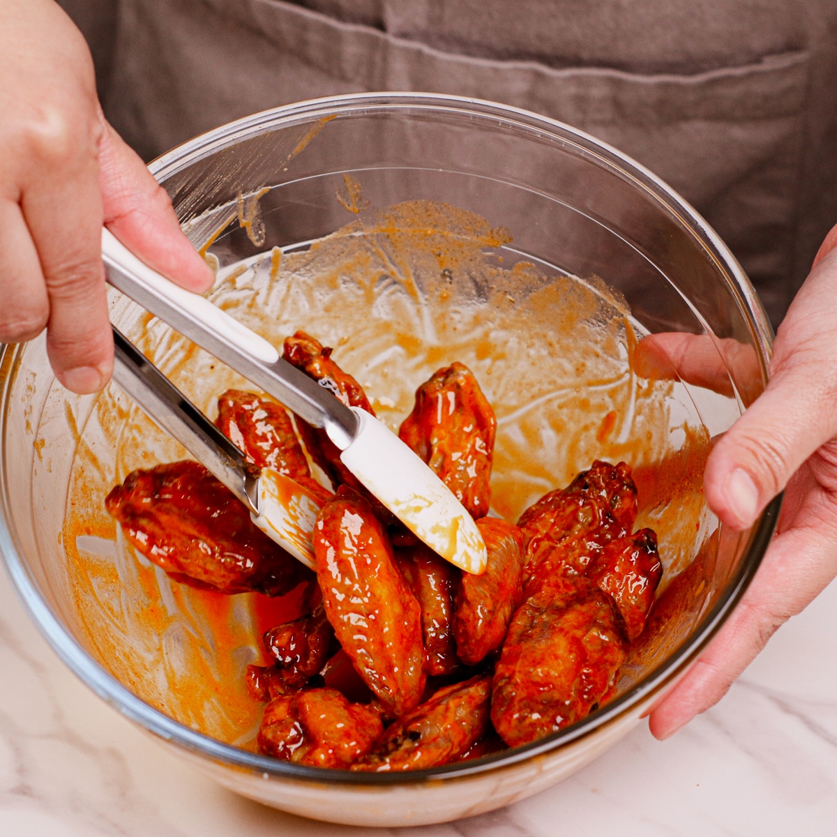 Coating air fried chicken wings with Buffalo sauce.