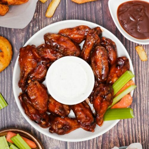 Air fryer BBQ chicken wings recipe bite shot, top view, served with sauce, celery, carrots, onion rings, soda and fries.