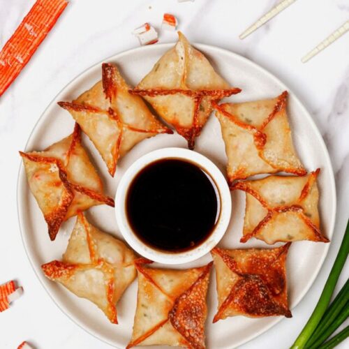 Air fryer crab rangoons recipe bite shot served on a plate with a side of dipping sauce.