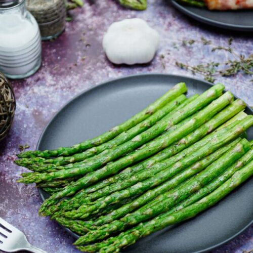 Air fryer garlic roasted asparagus recipe bite shot, served on a black plate with garlic on the background.