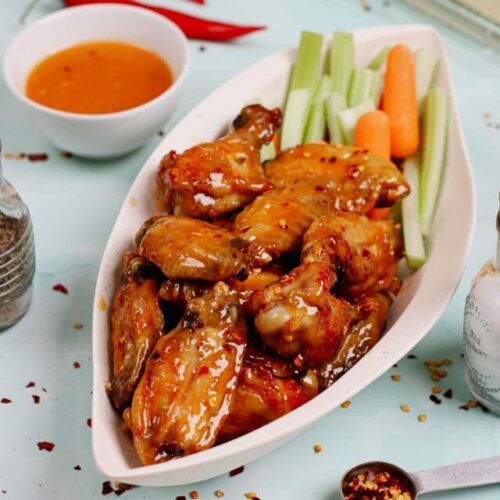 Air fryer honey hot wings recipe bite shot, served in a leaf-shaped serving dish with celery and carrot sticks on the side.