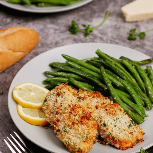 Air fryer parmesan crusted salmon recipe bite shot, with green beans and sliced lemons on the side.