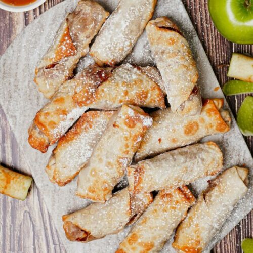 Apple pie egg rolls air fryer recipe bite shot with powdered sugar on top and caramel dipping sauce.