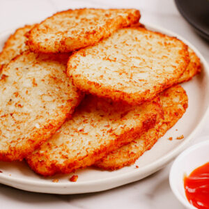 Air fryer frozen hash browns served on a plate with ketchup on the side.