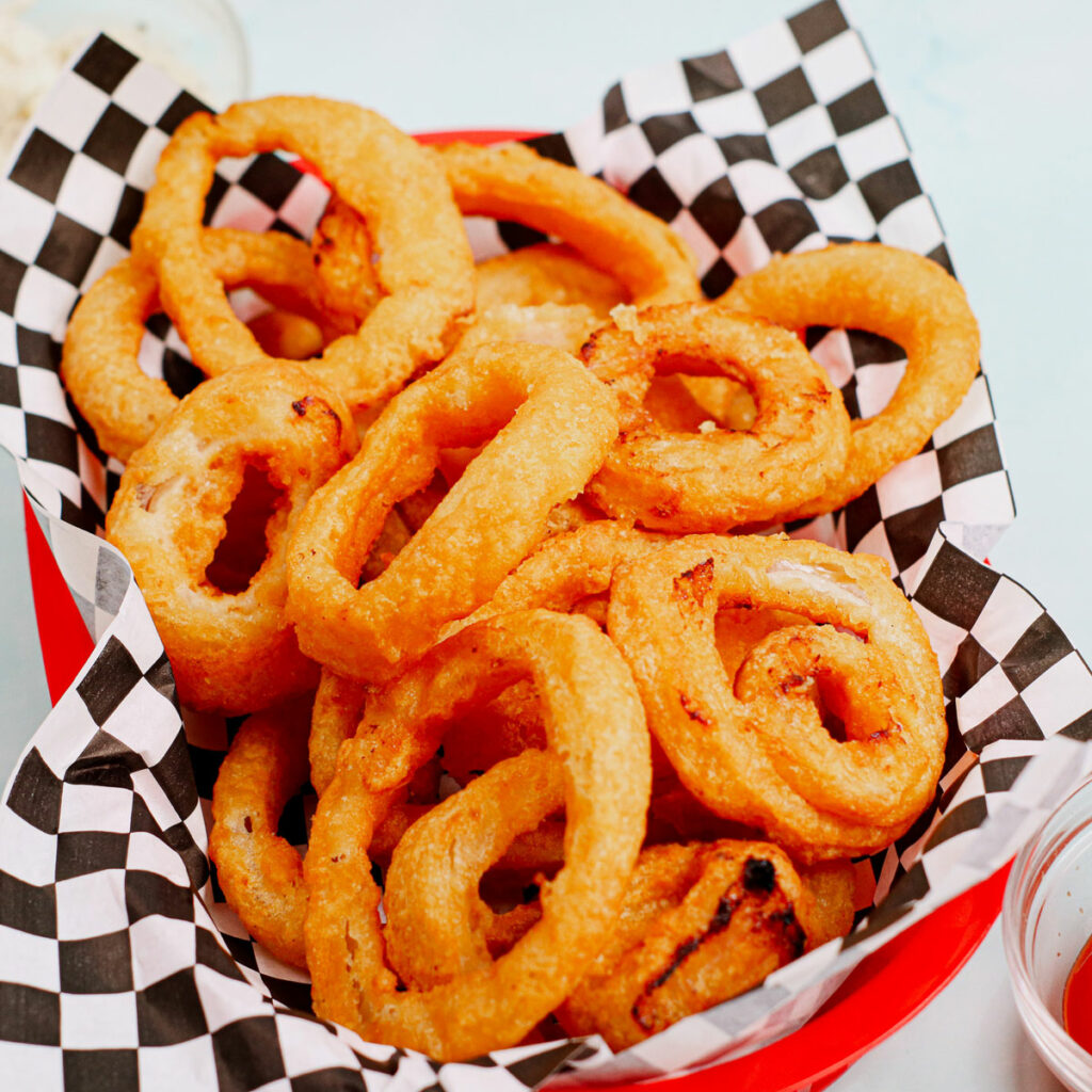 Air fryer frozen onion rings in a traditional fast food tray with checkered parchment paper.