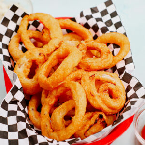 Air fryer frozen onion rings in a traditional fast food tray with checkered parchment paper.