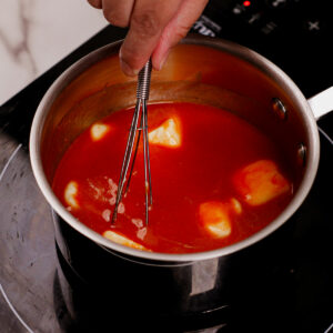 Stirring Buffalo sauce mixture in a small pot.