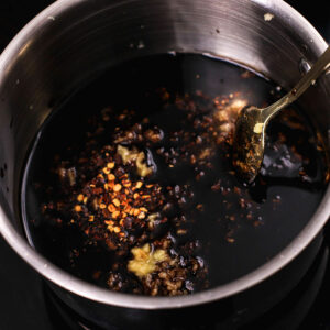 Reducing honey garlic sauce in a small pot, with a spoon.