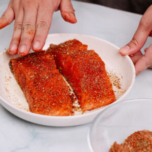 Rubbing salmon filets with cajun seasoning.