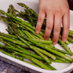 Seasoning asparagus with olive oil, crushed garlic, salt and pepper.