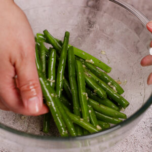 Seasoning french green beans in a large glass bowl