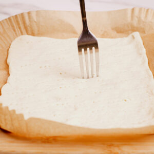 Docking pizza dough with fork.