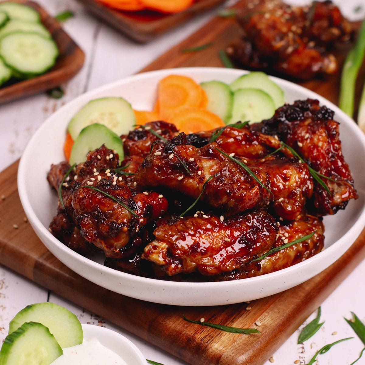 Air fried mongolian chicken wings on a white plate with sliced carrots and cucumbers on the side.