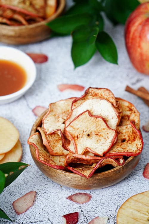 Air fryer apple chips recipe bite shot, served in a small wooden bowl with caramel dipping sauce on the side.