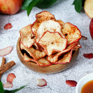 Air fryer apple chips served in a small wooden bowl with caramel dipping sauce on the side.