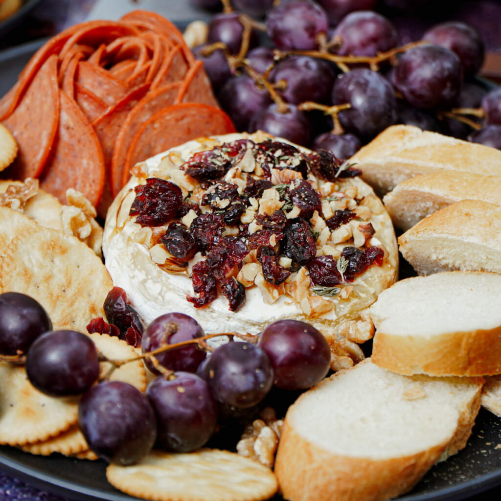 Air Fryer Baked Brie with baguette slices, grapes, crackers, and pepperoni.