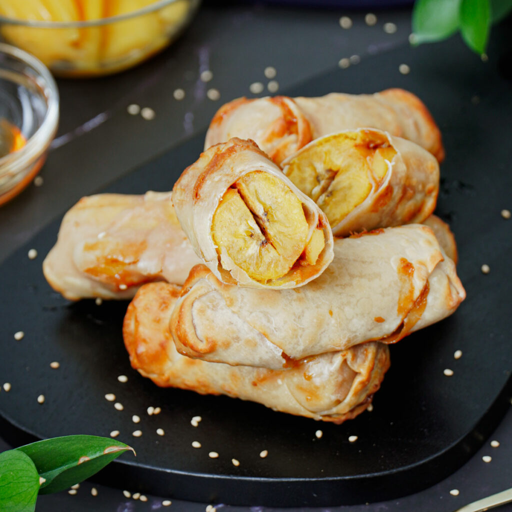 Stacked air fryer banana egg rolls on a black serving board.